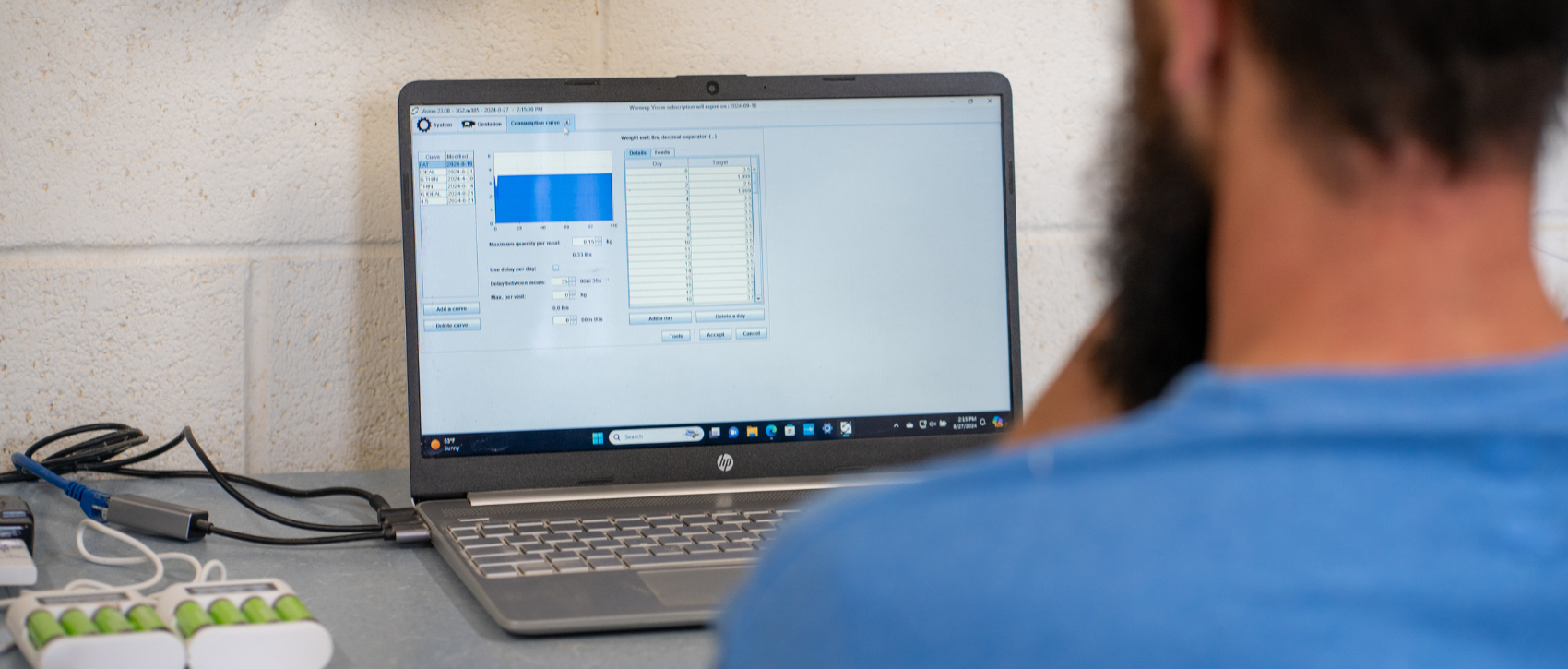 Person using a laptop with a screen displaying software interface in a pig barn